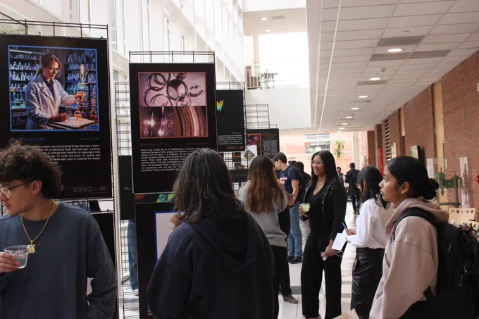 People gathered in an atrium where Science as Art entries are set up, the people are chatting and looking at the art.