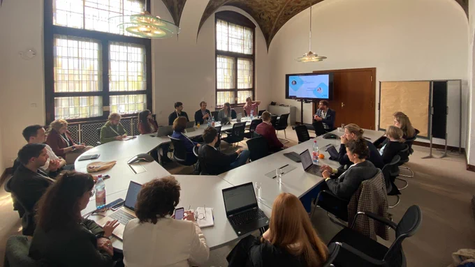Präsentationsrunde beim UrbanDataSummit in Leipzig: Zu sehen sind ca. 20 Menschen an einem U-förmigen Konferenztisch, im Hintergrund die Präsentation. Foto: DKSR