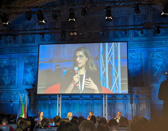 A woman speaking on a big screen in a beautiful old building