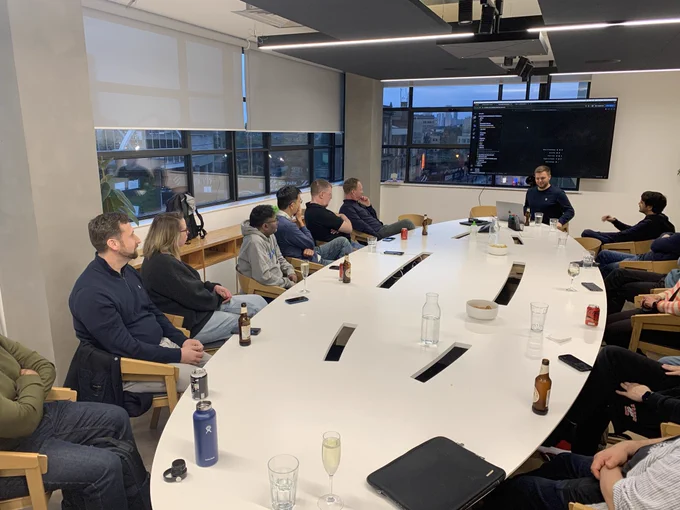 People sitting round a boardroom table looking at the presenter sharing code on the big screen