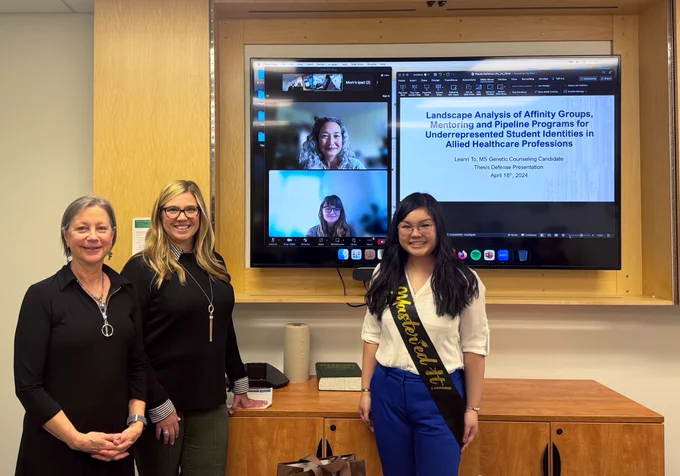 Leann and her thesis committee standing in front of a TV monitor showing powerpoint title slide "Landscape Analysis of Affinity Groups, Mentoring and Pipeline Programs for Underrepresented Student Identities in Allied Healthcare Professions"