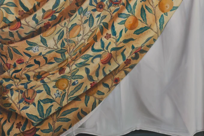 A painting of a cloth, with a pattern of flowers and fruit, draped over another plain white cloth.
