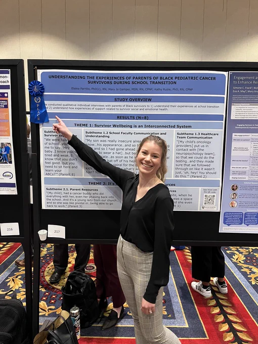 Laina stands in front of her winning poster pointing to the blue first place ribbon.