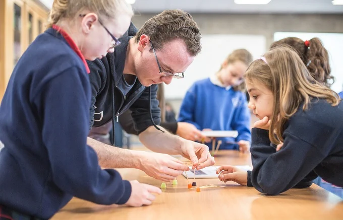 
Teacher and young students in a classroom, working together on a project
