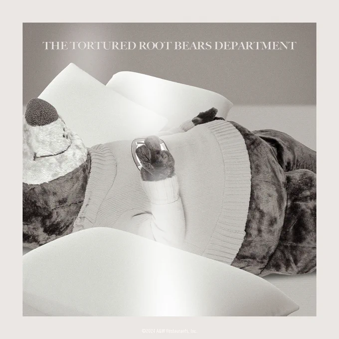 Black and white photo of Rooty the Great Root Bear laying on a bed with pillows. Text above Rooty reads "The Tortured Root Bears Department"