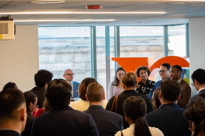 Top view behind a large crowd listening to a group of four staffers speaking 