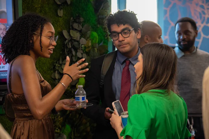 Young woman wearing glasses gestures emphatically while speaking to a young man and woman 