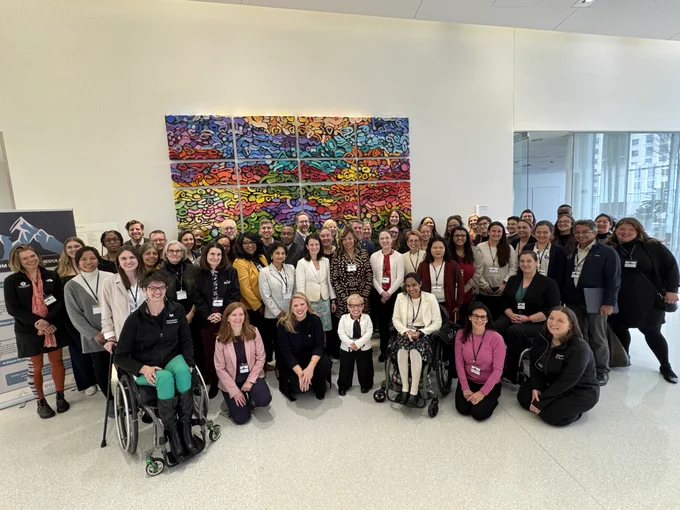Large group of people with varied disabilities in front of a colorful panel