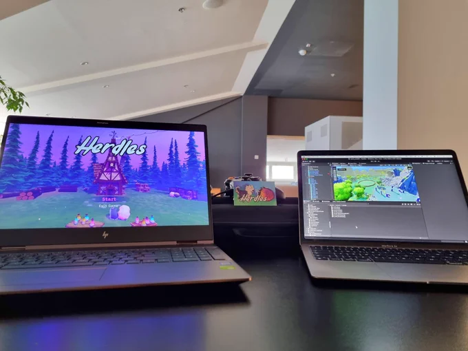 Two laptops on a desk showing the game Herdles in a hotel setting. 
