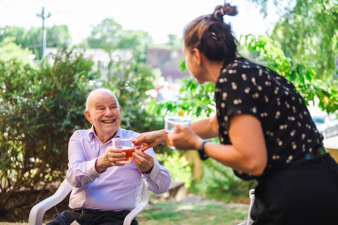 An image of a carer helping an older man, in a garden setting.