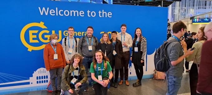 Photo of members of the UK Polar Network committee stood in front of a blue Welcome to the EGU General Assembly 2024 banner