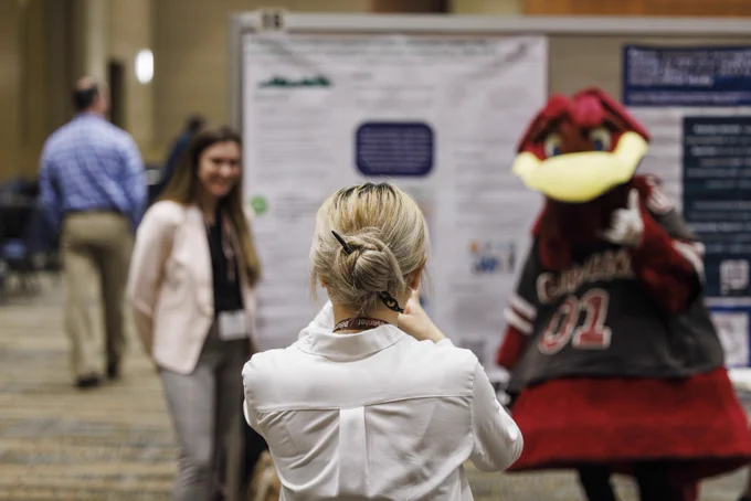 Making memories: A Discover USC presenter snaps a photo of her co-presenter, posing with Cocky at their poster.