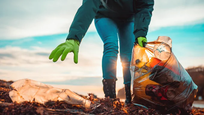 a person picking up plastic litter from outside with a bag full of plastic already gathered