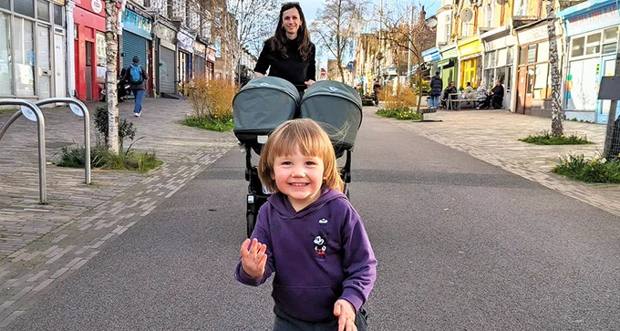 A woman pushing a double pushchair and a little boy walking in a pedestrianised shopping area.