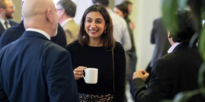 woman holding a cup of coffee smiles while in conversation with a man with back towards the camera
