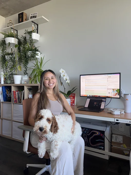 Woman and dog sitting in a char smiling with a home office setup in the background.