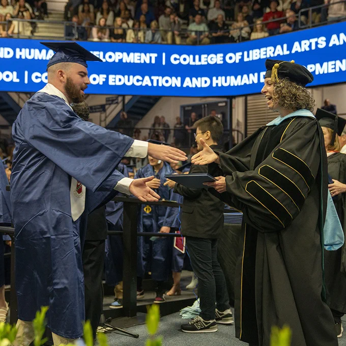 University of Maine College of Education and Human Development dean Penny Bishop shakes hands with a new graduate during the 2024 commencement ceremony.
