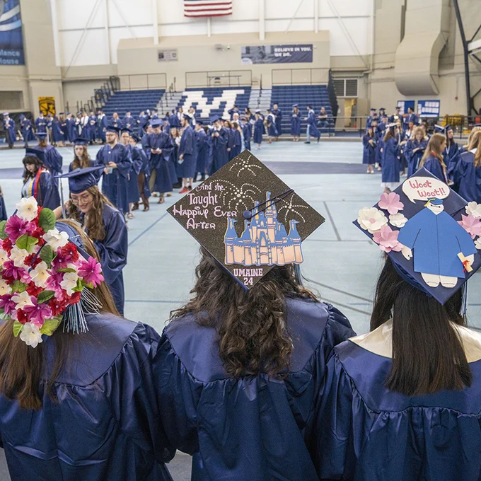University of Maine College of Education and Human Development students show off their decorated mortarboards before the 2024 commencement ceremony. One says, "And she taught happily ever after, UMaine 24."