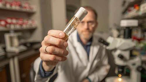Jeremiah Zartman in a lab holding a test tube close to the camera
