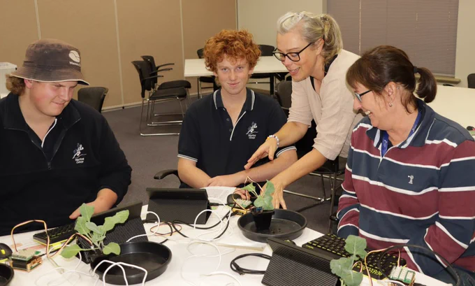 Students from Murtoa College with instructor and teacher looking at Raspberry Pi computers, moisture sensors and vegetable pots on table.
