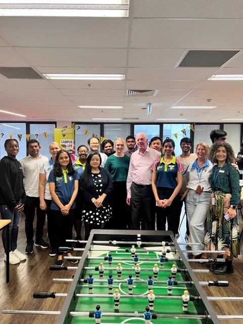 Chancellor Graeme Innes pictured with a group of 17 people smiling for a photo at University Mental Health Day in Brisbane.