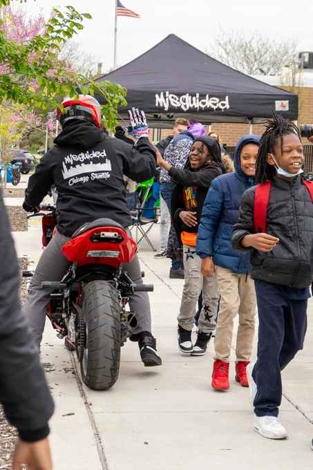 Students at Melody STEM high-five a man on a dirt bike as he passes by a crowd of students on a sidewalk 