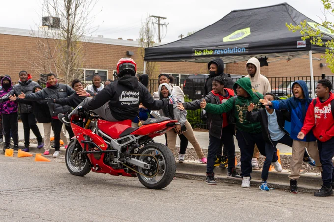 Students at Melody STEM high-five a man on a dirt bike as he passes by a crowd of students.