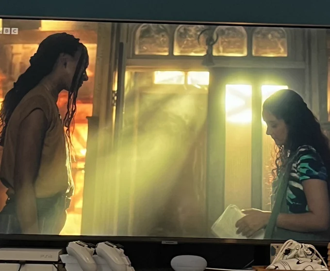 A still from A Kind of Spark in which Addie and Audrey stand in a dimly lit bookshop, dust pouring around them