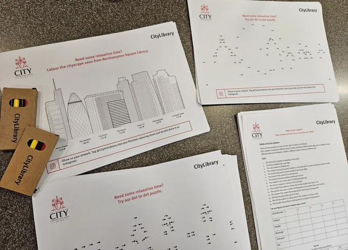 A colouring sheet with a City silhouette and colouring pencils nearby, as well as some dot-to-dot puzzles and a riddle on a printed paper.