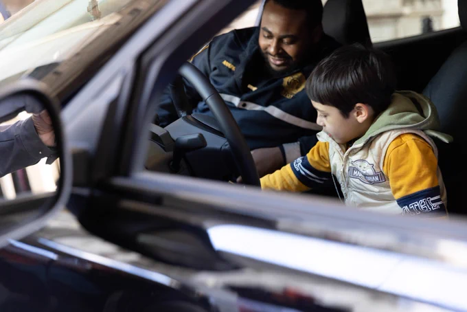 Child sits behind the wheel of an electric vehicle with a fleet staff member.  