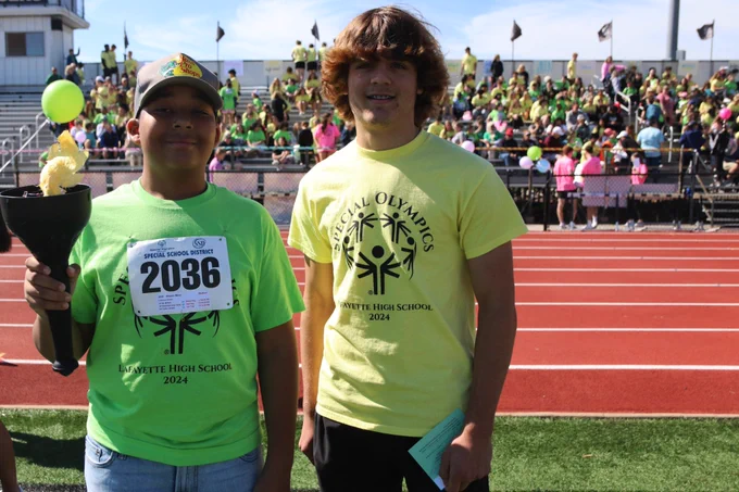 Students smile as they participate, including one holding the torch, in the Special Olympics track and field event at a Rockwood school.