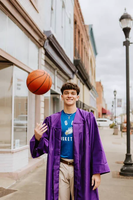 a student wearing an FGCU shirt and grad gown tosses a basketball in the air
