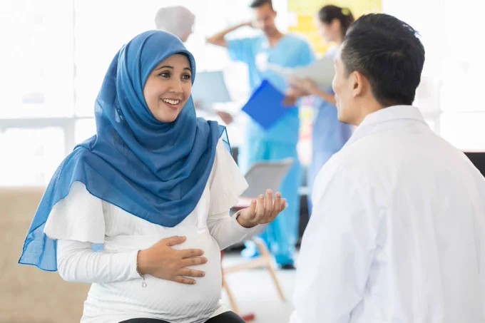 Photo of a pregnant woman who is wearing a hijab speaking with a doctor.