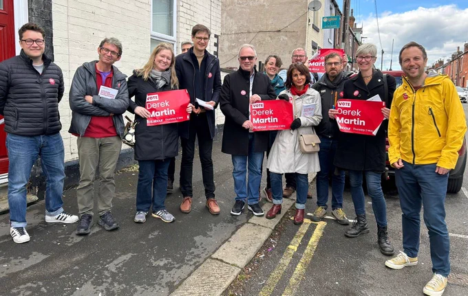 A photo of twelve Labour Party campaigners on a street in Sharrow. Some people are holding up posters that say 'Vote Derek Martin'.