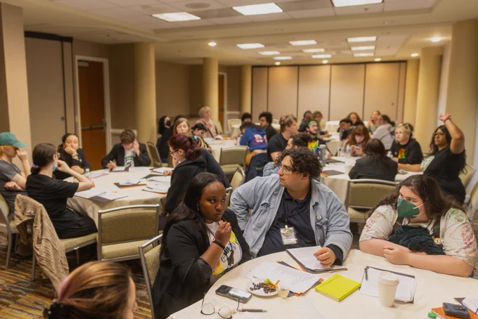 About 20 Starbucks Workers United members deliberate in a room, some with their hands up
