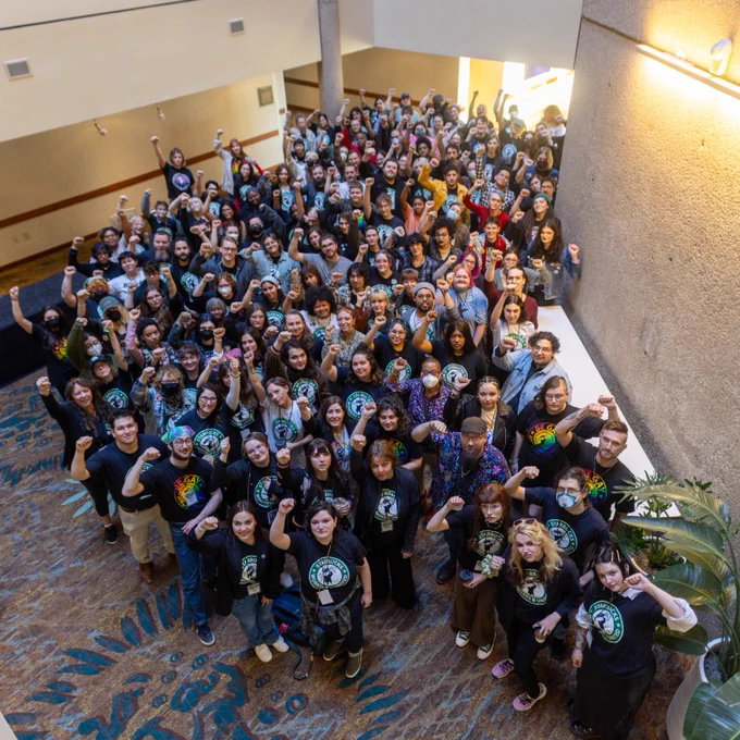 A large group of Starbucks Workers United members look up and pose with their fists in the air