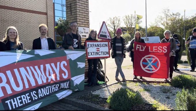 Cllr Jonathan Essex and Sian Berry with a Green Party banner saying ‘No new runways’ outside the hotel hosting the Gatwick expansion examination hearing, alongside campaigners with XR banners and homemade placards saying ‘expansion = extinction’ and ‘fly less’