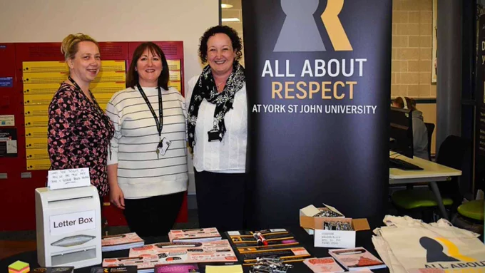 3 people at an information stall with leaflets and merchandise. 