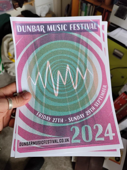 A hand holds a small poster with an abstract sound wave design advertising Dunbar Music Festival