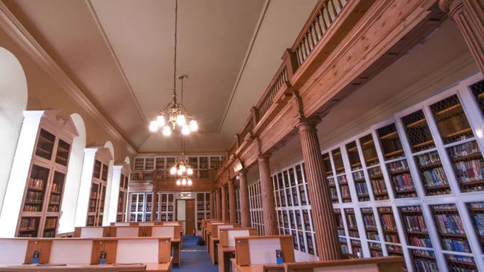 1: Library of the Week - King James Library, Scotland. 2: a light library, with floor-ceiling bookshelves, white book cabinets, a balcony, and reading tables.