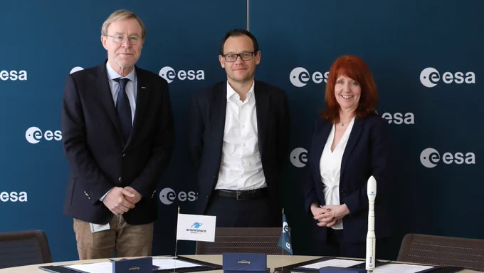 Three people standing in front of contracts. The background wall is covered in ESA logos