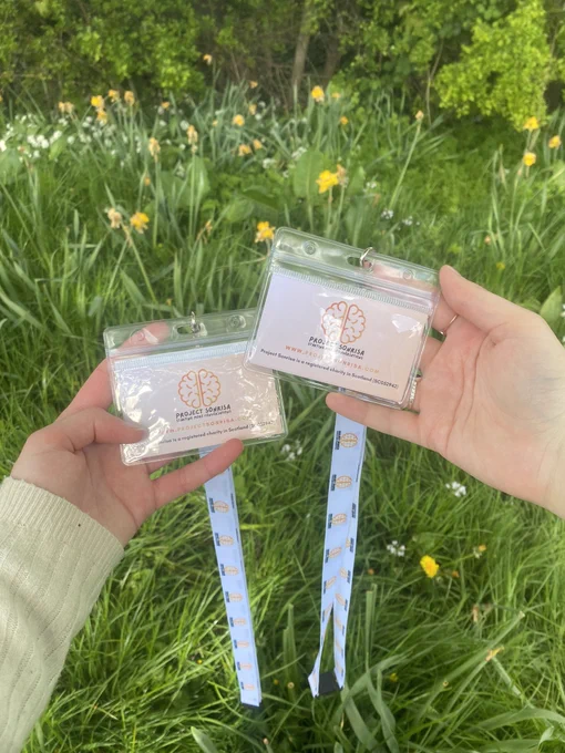 Two hands holding Project Sonrisa lanyards against a backdrop of grass and daffodils.