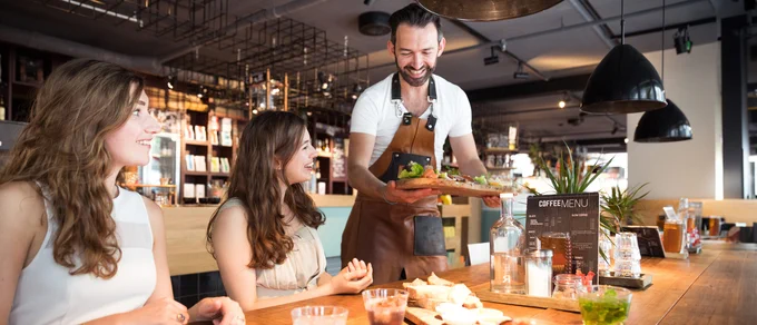 Women sitting at a restaurant. Waiter serving food. 