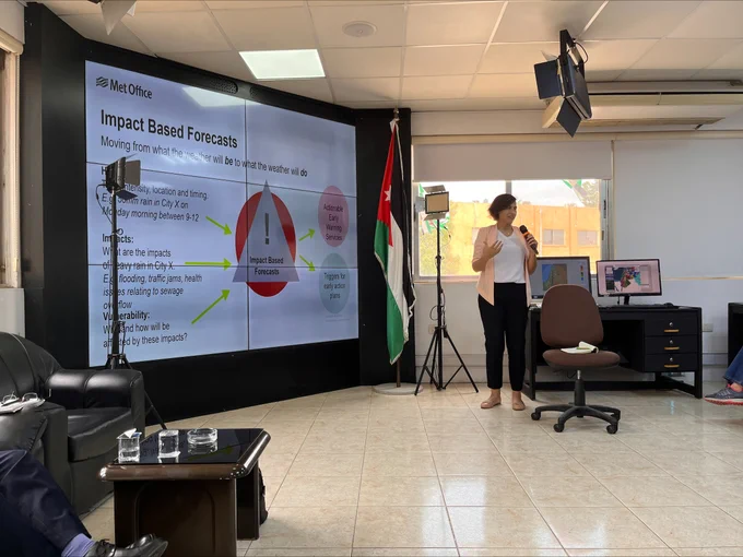 Female presenter delivering a presentation entitled Impact Based Forecasts on a large screen.