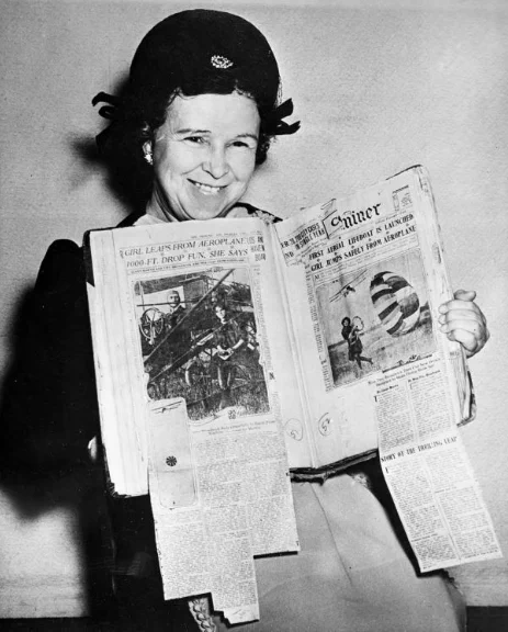 Black and white: older woman holding a scrapbook displaying newspaper clippings