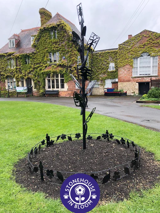 Black metalwork tree with old shovel, spades and trowels for leaves. On the green outside the High Street Medical Centre.