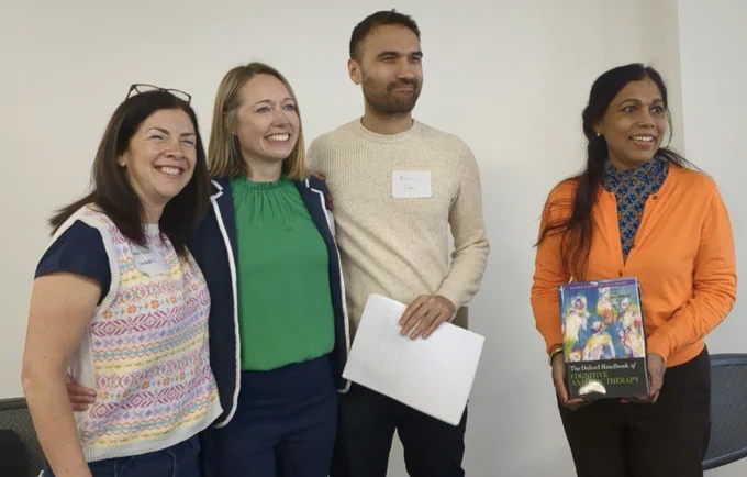Marisol Cavieres, Laura Brummer and Ranil Tan stand together smiling as Jessie Emilion, ACAT Chair, holds a copy of the Oxford Handbook of Cognitive Analytic Therapy beside them
