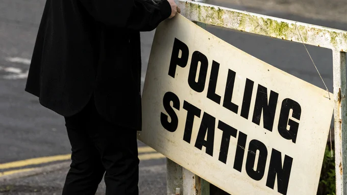 A person putting up a sign that reads 'POLLING STATION' 