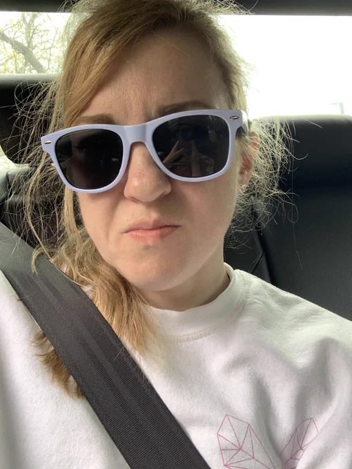 Blonde haired woman wearing sunglasses and a white sweatshirt looking uneasy