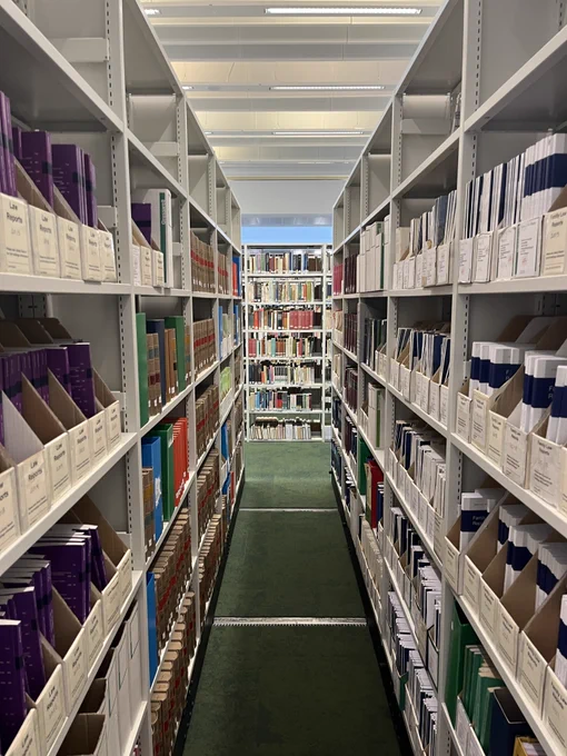 Three bookshelves, two facing each other, one at the opposite end to the picture taker. 
